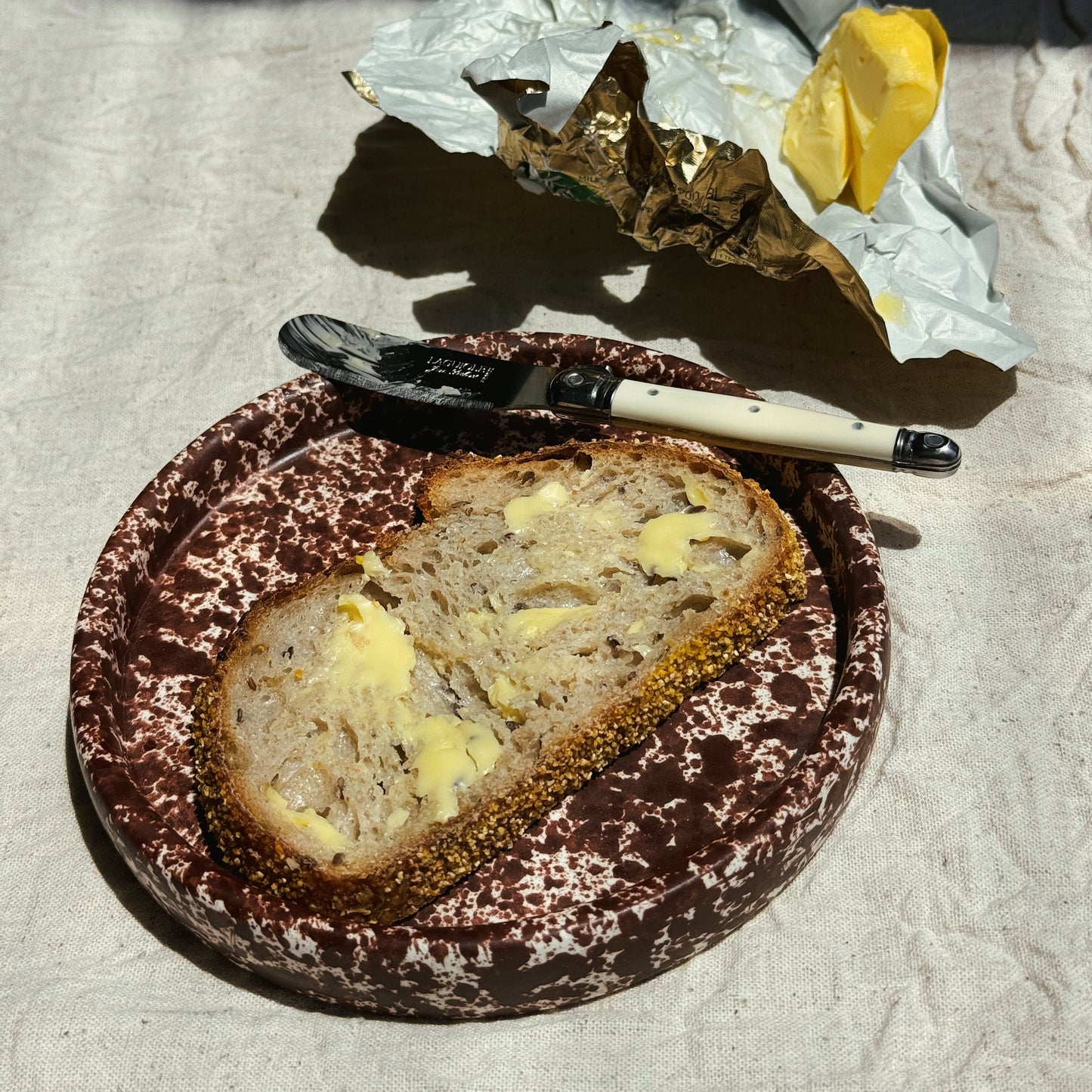 Sliced bread with butter on a plate with a fork and knife, on a textured surface. Stoneware handmade ceramic plates, dessert plates.