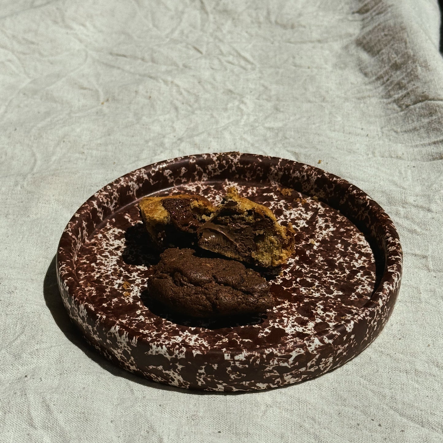 Chocolate cookie with a bite taken out on a textured surface. Stoneware handmade ceramic plates, dessert plates.