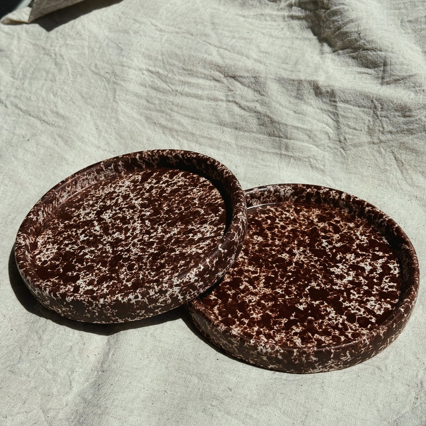 Two round brown ceramic plates on a textured light fabric surface. Stoneware handmade ceramic plates, dessert plates.
