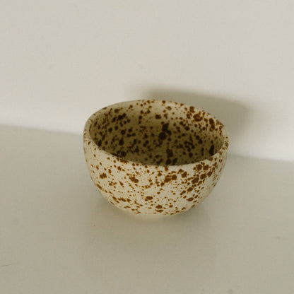 Small ceramic bowl with brown speckles on a light beige background