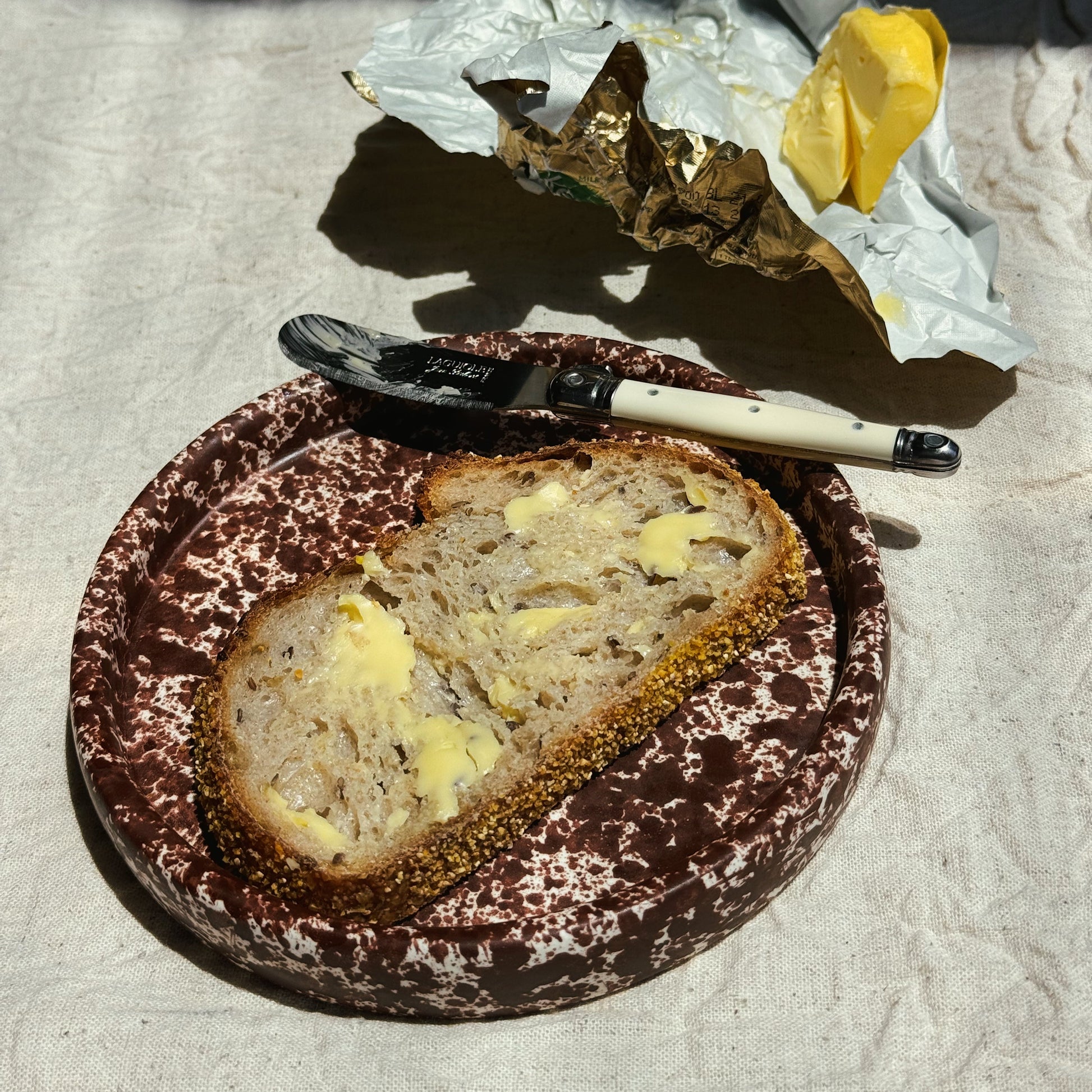 Sliced bread with butter on a plate with a fork and knife, on a textured surface. Stoneware handmade ceramic plates, dessert plates.