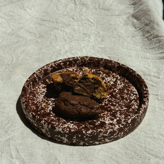 Chocolate cookie with a bite taken out on a textured surface. Stoneware handmade ceramic plates, dessert plates.