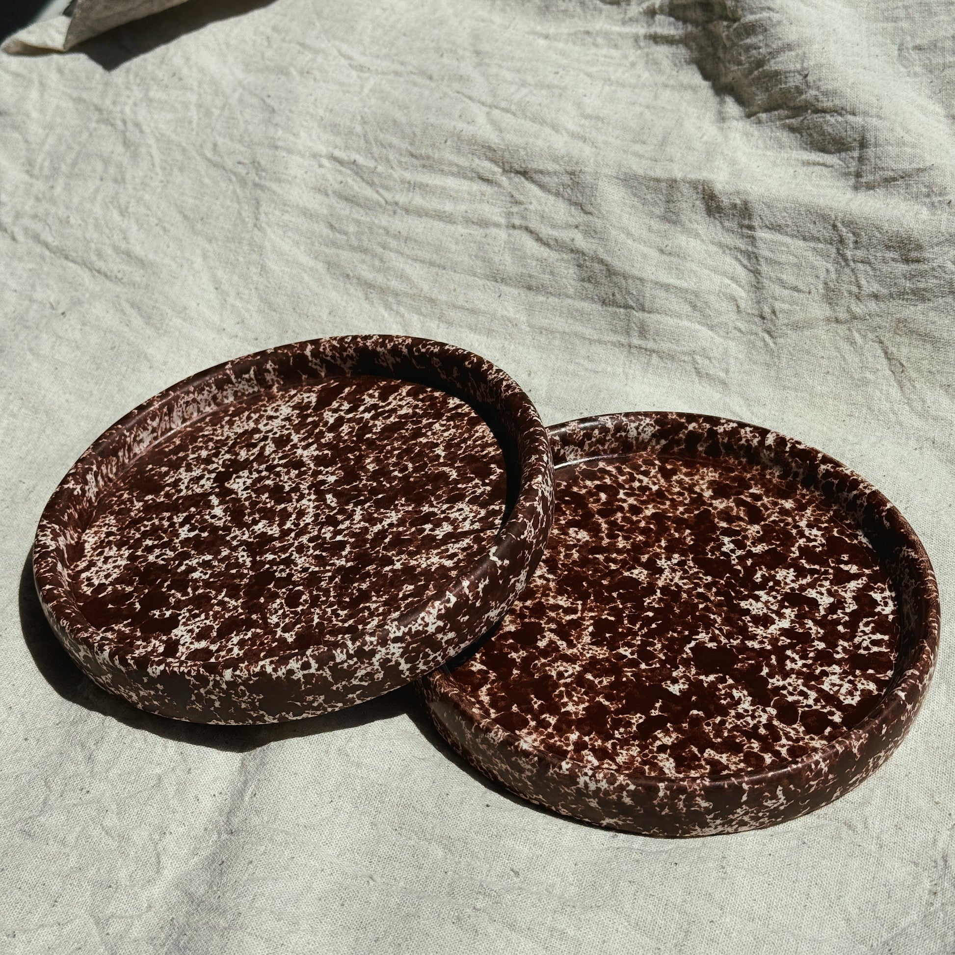 Two round brown ceramic plates on a textured light fabric surface. Stoneware handmade ceramic plates, dessert plates.
