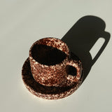 Copper mug and saucer casting a shadow on a light gray background. Handmade ceramic mug set, burgundy, fall colors. Handmade coffee mug.