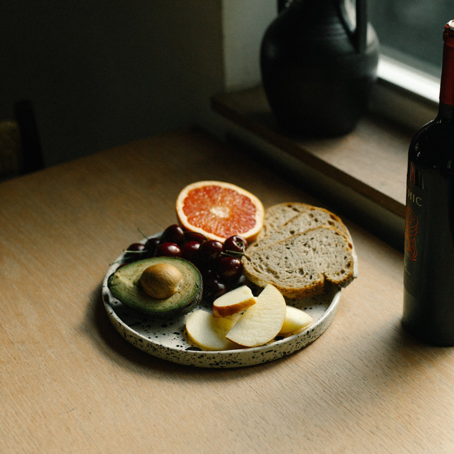 Small plate with sliced bread, avocado, and fruit on a wooden surface near a window. handmade ceramic platter, dinner plate, modern stoneware casa azua