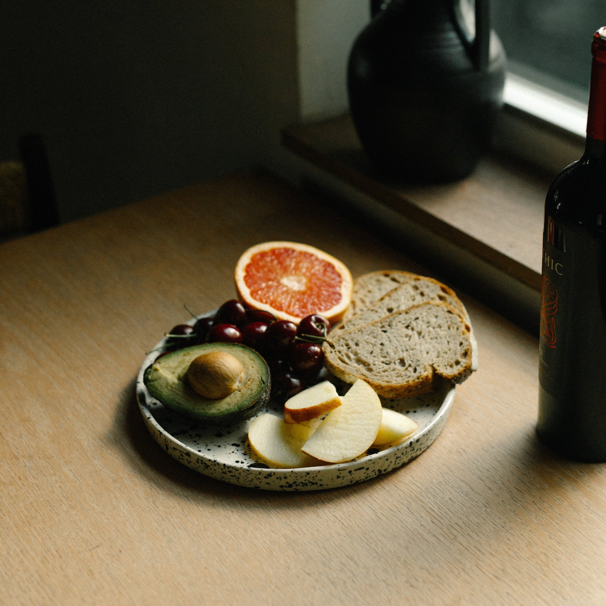 Small plate with sliced bread, avocado, and fruit on a wooden surface near a window. handmade ceramic platter, dinner plate, modern stoneware casa azua
