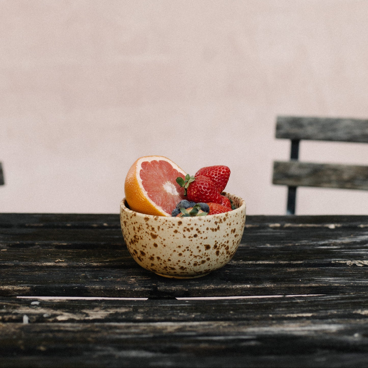 Small speckled ceramic bowl with fruits on a wooden table against a plain background
