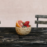 Small speckled ceramic bowl with fruits on a wooden table against a plain background