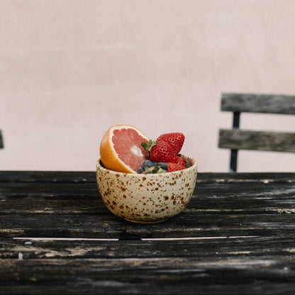 Small speckled ceramic bowl with fruits on a wooden table against a plain background