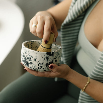 Making matcha, with cute matcha set. Person holding a small speckled bowl with a wooden tool, wearing a striped sweater.