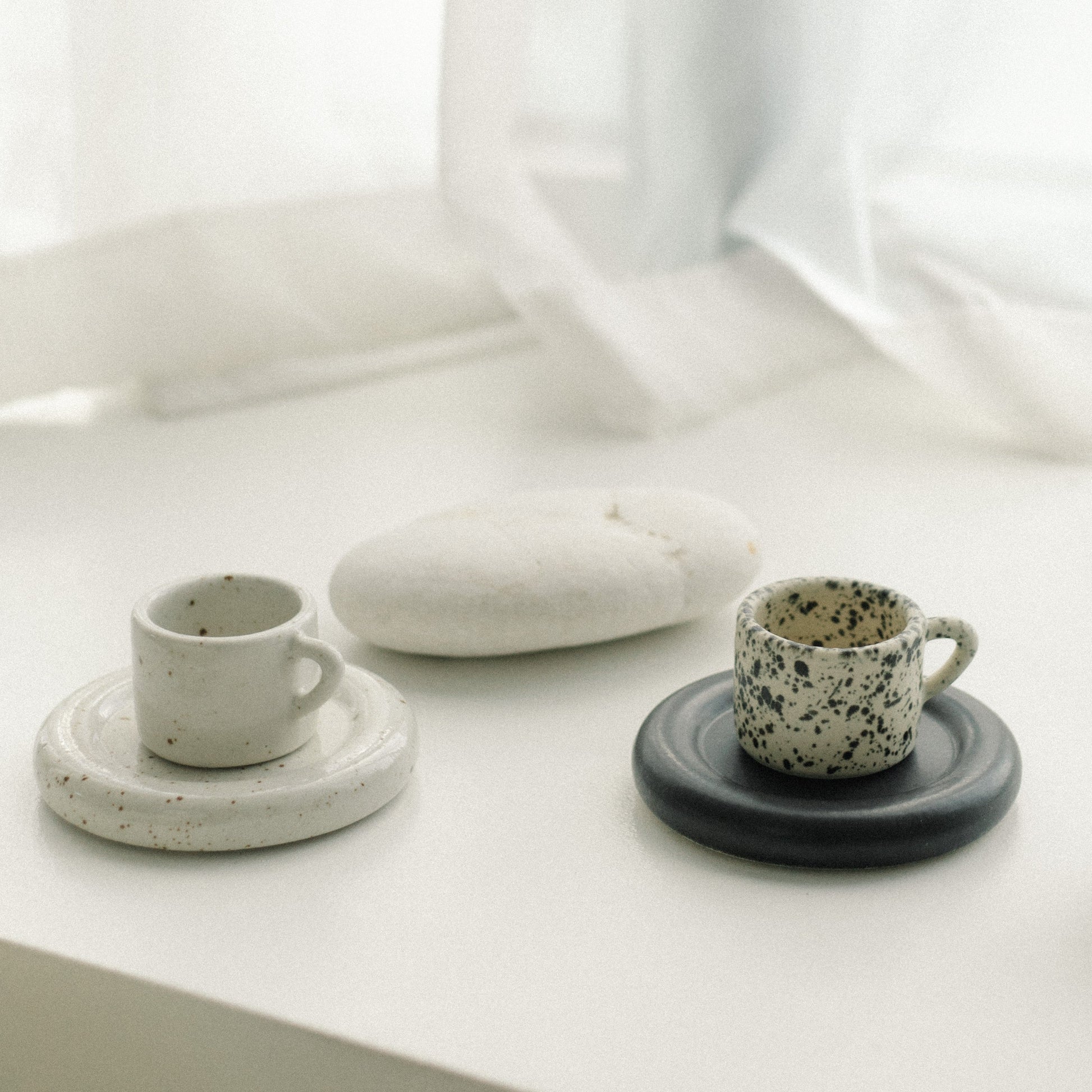 Ceramic cups and bowls on a white surface with sheer curtains in the background