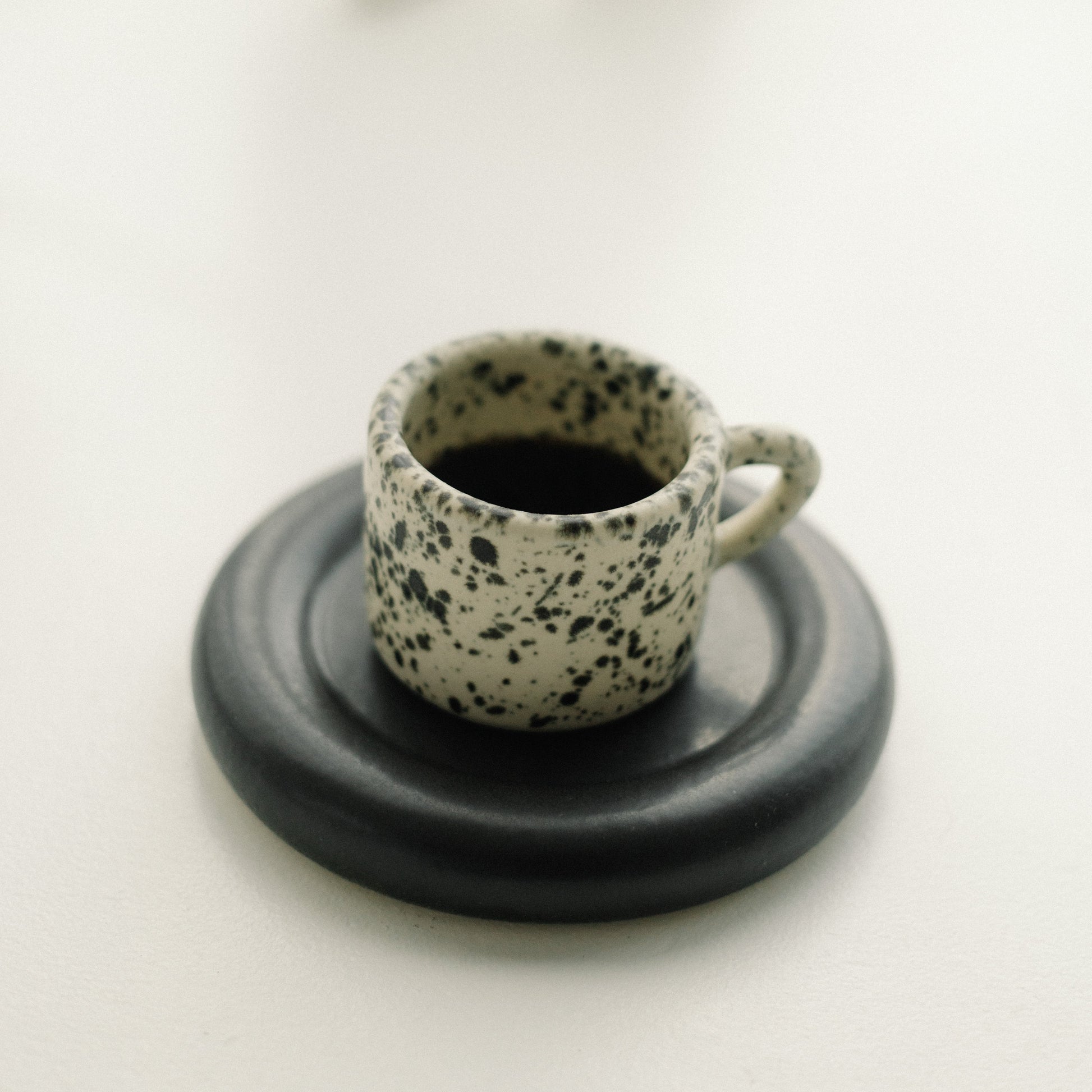 Speckled ceramic cup with black interior on a matching saucer on a white surface